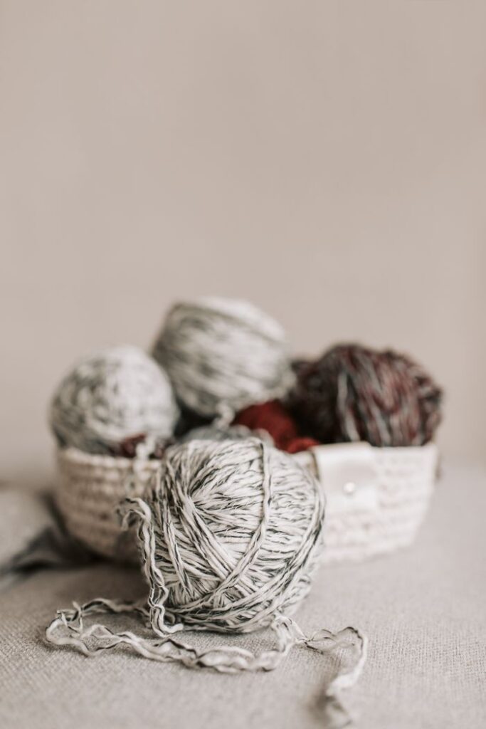 A detailed shot of colorful yarn balls arranged in a knitted basket on a neutral background.